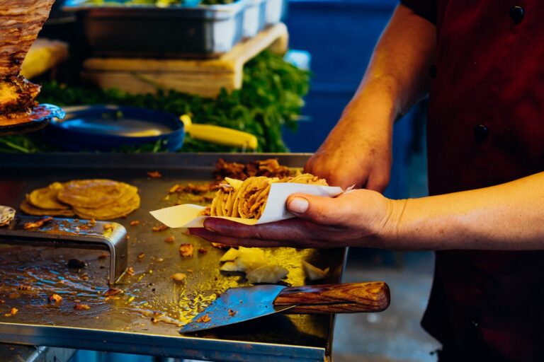 Taquero carving al pastor pork from the trompo onto a corn tortilla