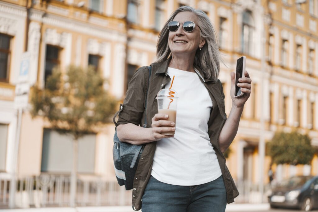 Woman traveling alone in an old town, smiling, with a coffee and her phone